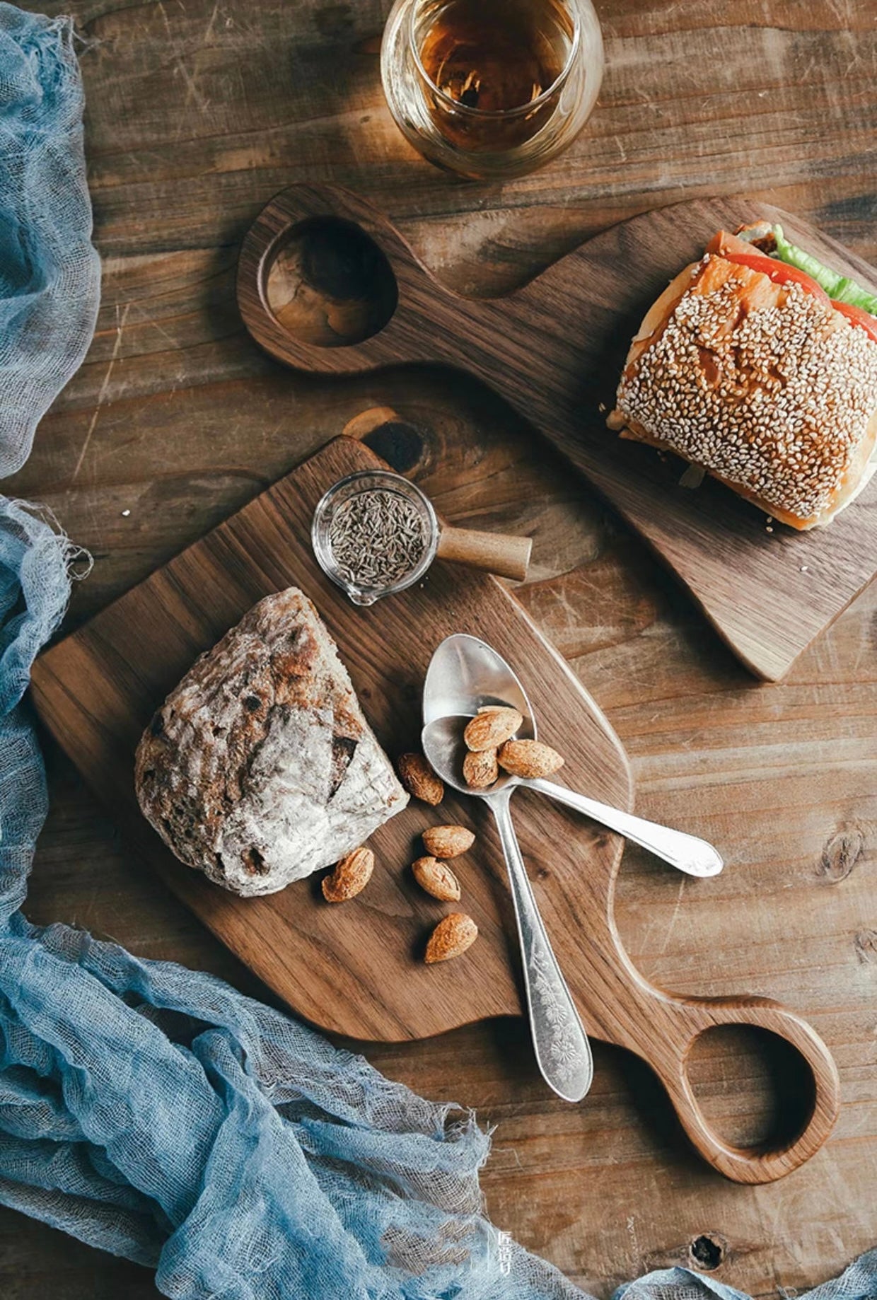 Black walnut cutting board styled as a charcuterie board with bread, almonds, and a drink glass on a rustic wooden table