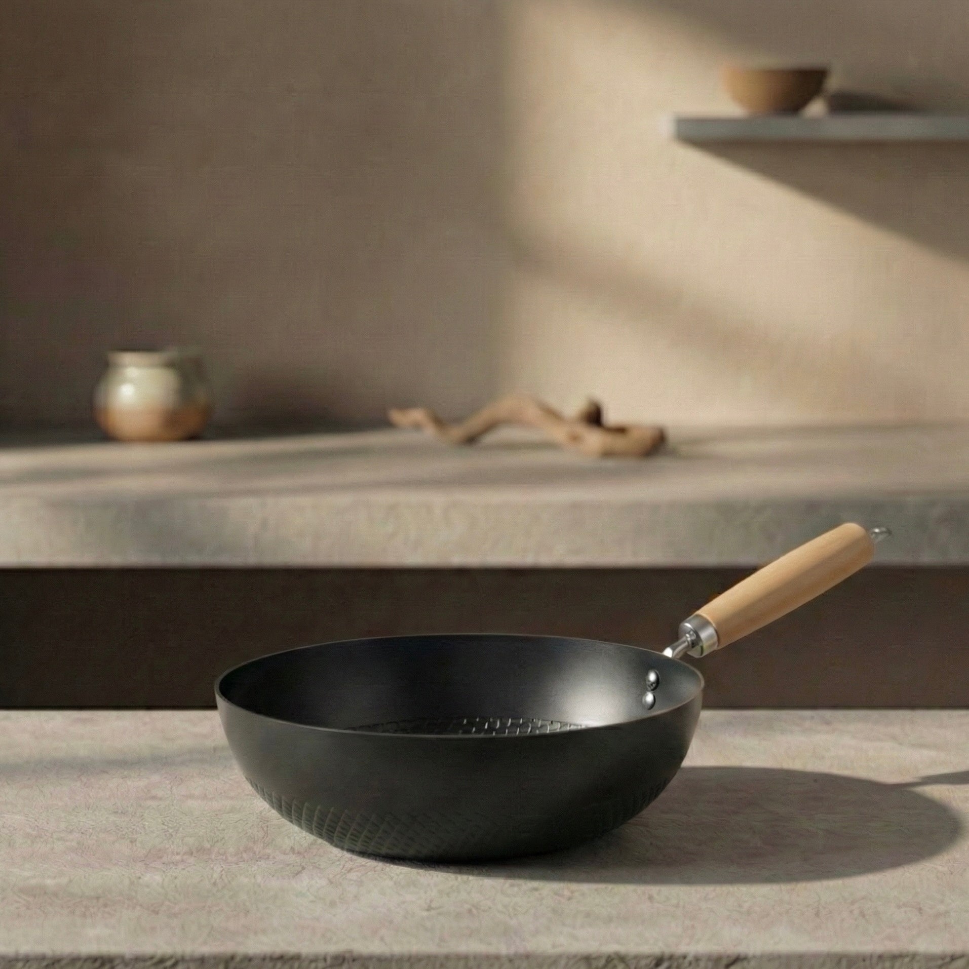Black nitride iron 22cm Solo Wok with wooden handle resting on a stone surface in warm natural light