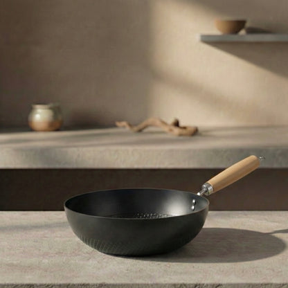 Black nitride iron 22cm Solo Wok with wooden handle resting on a stone surface in warm natural light