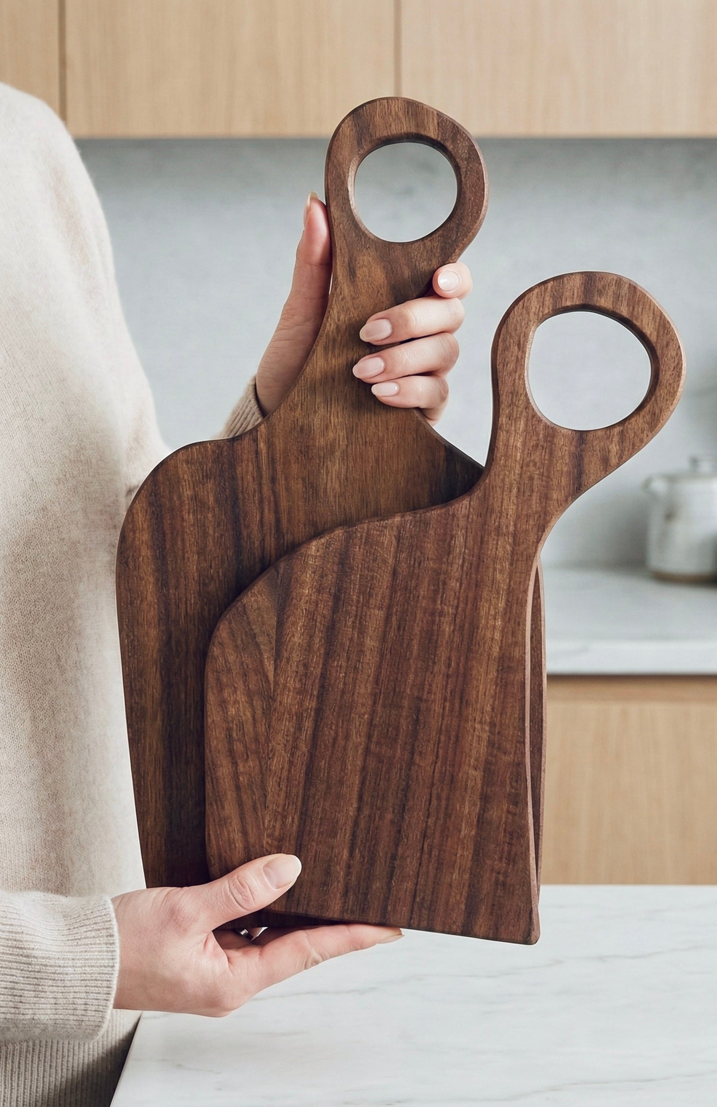 Person holding two black walnut cutting boards of different sizes in a bright kitchen