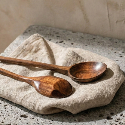Two natural Phoebe wood cooking spoons laid on cream linen fabric